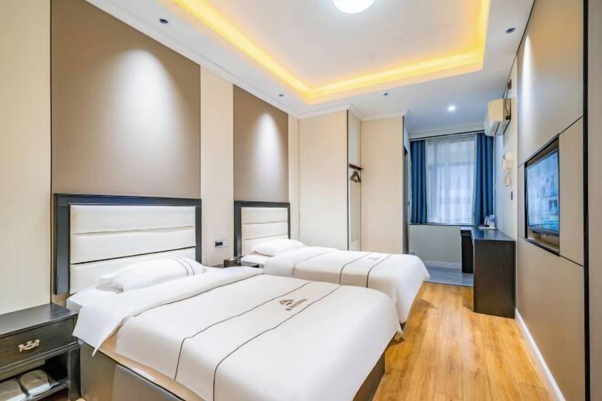 A hotel room with two beds, a desk, a TV, and a window with curtains.