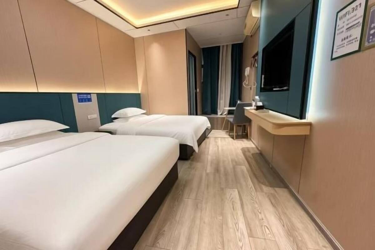 A hotel room with two beds, a desk, a TV, and a sign indicating WiFi availability.