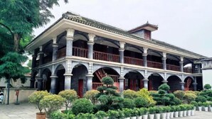 A traditional building with multiple balconies and a tiled roof, surrounded by a well-maintained garden with various plants.