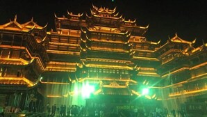 A traditional multi-tiered building with illuminated upper levels and a crowd gathered at the base.