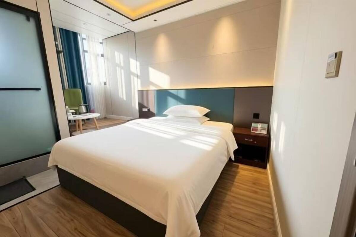 A hotel room with a large bed, a bedside table, a chair, and a desk.