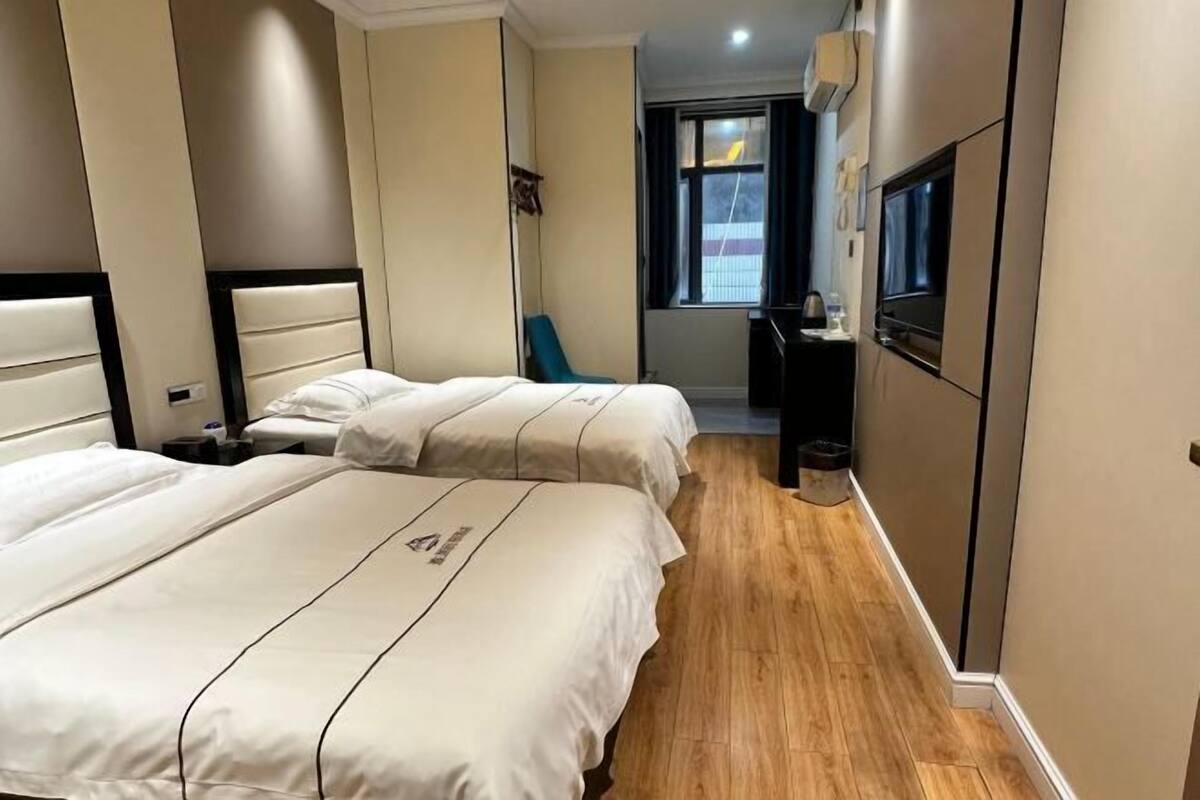 A hotel room with two beds, a small seating area, a window, and a TV.
