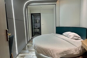 A modern bedroom with a curved wall, a bed with white bedding, a wooden nightstand, and a bathroom visible through an open door.