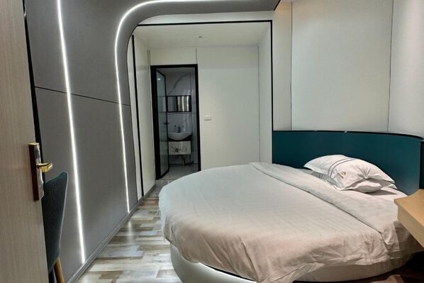 A modern bedroom with a curved wall, a bed with white bedding, a wooden nightstand, and a bathroom visible through an open door. - Yaju Homestay Hotel (Zunyi Conference Site) (Zunyi)