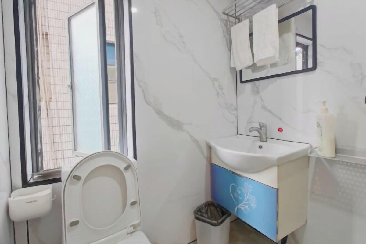 A bathroom with a toilet, sink, mirror, and a trash bin.