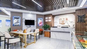 A modern hotel lobby with a reception desk, seating area, and a large screen displaying content.