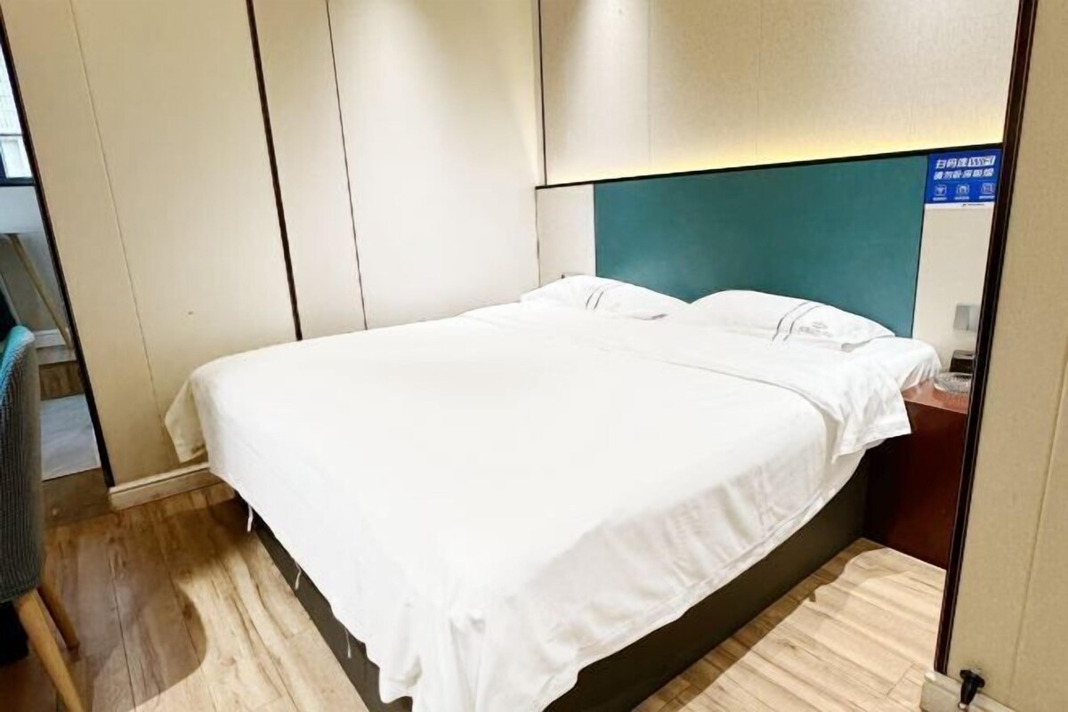 A hotel room with a bed, wooden flooring, and a teal-colored headboard.