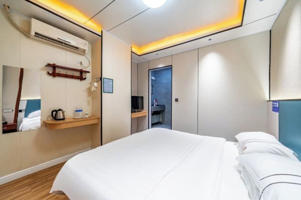 A hotel room with a bed, a bedside table with a kettle, a mirror, and a wardrobe.