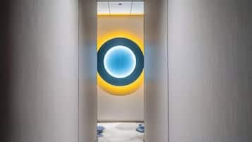 A corridor with a circular light fixture on the wall, a carpeted floor, and a door at the end.