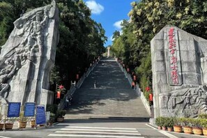 Una escalera conduce a un monumento de piedra con inscripciones, rodeado de árboles y plantas en macetas.