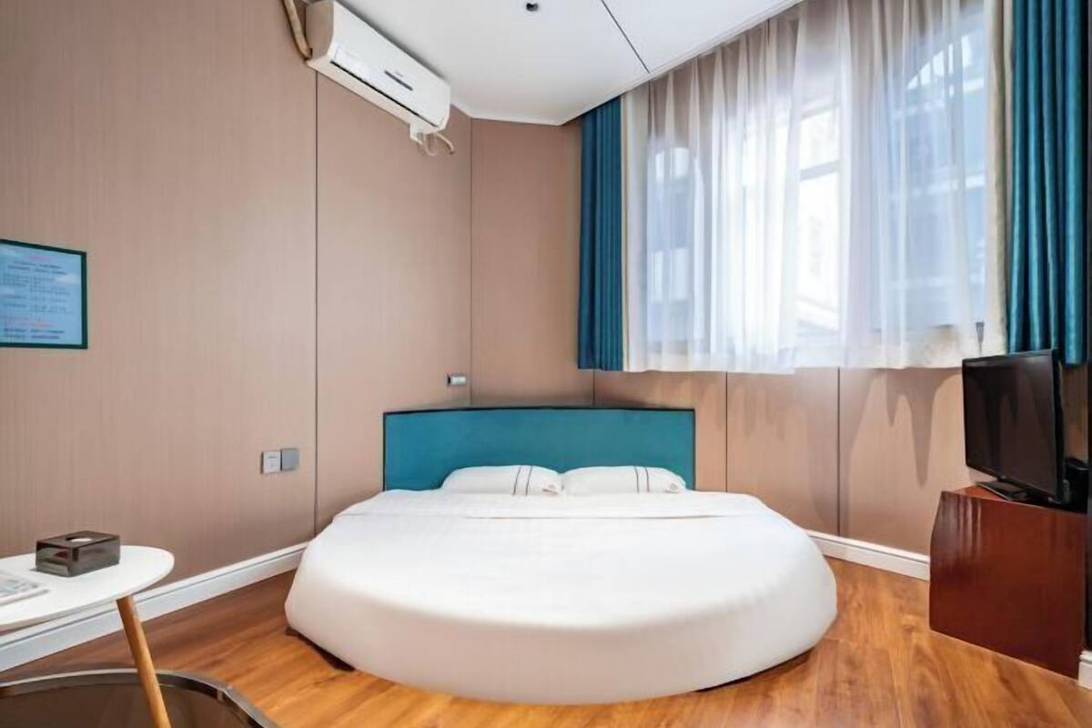 A modern hotel room with a round bed, a television, and a small desk with a chair.