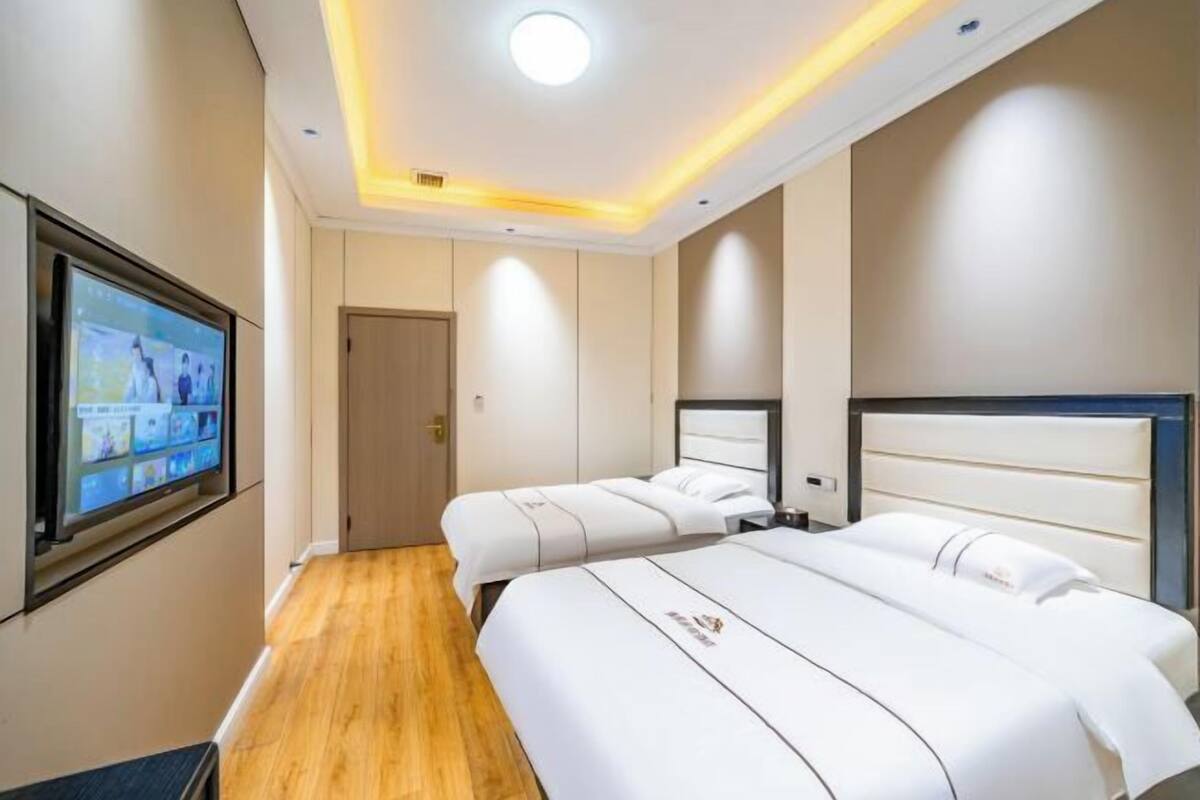 A hotel room with two beds, a TV on the wall, and a wooden floor.