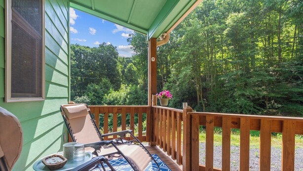 A wooden deck with two lounge chairs and a table, overlooking a forested area.