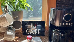 A kitchen counter with a coffee maker, a sign reading "THE CAFE", and a tray with cups and a jar of cinnamon.