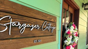 A wooden sign with "Stargazer Cottage" and "EST 2024" on a green building facade.