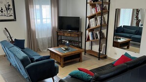 Un salon avec un canapé, une table basse, un téléviseur, une bibliothèque et un miroir.