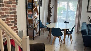 Un salon avec un escalier, un coin repas avec une table et des chaises, une bibliothèque et une vue par la fenêtre.