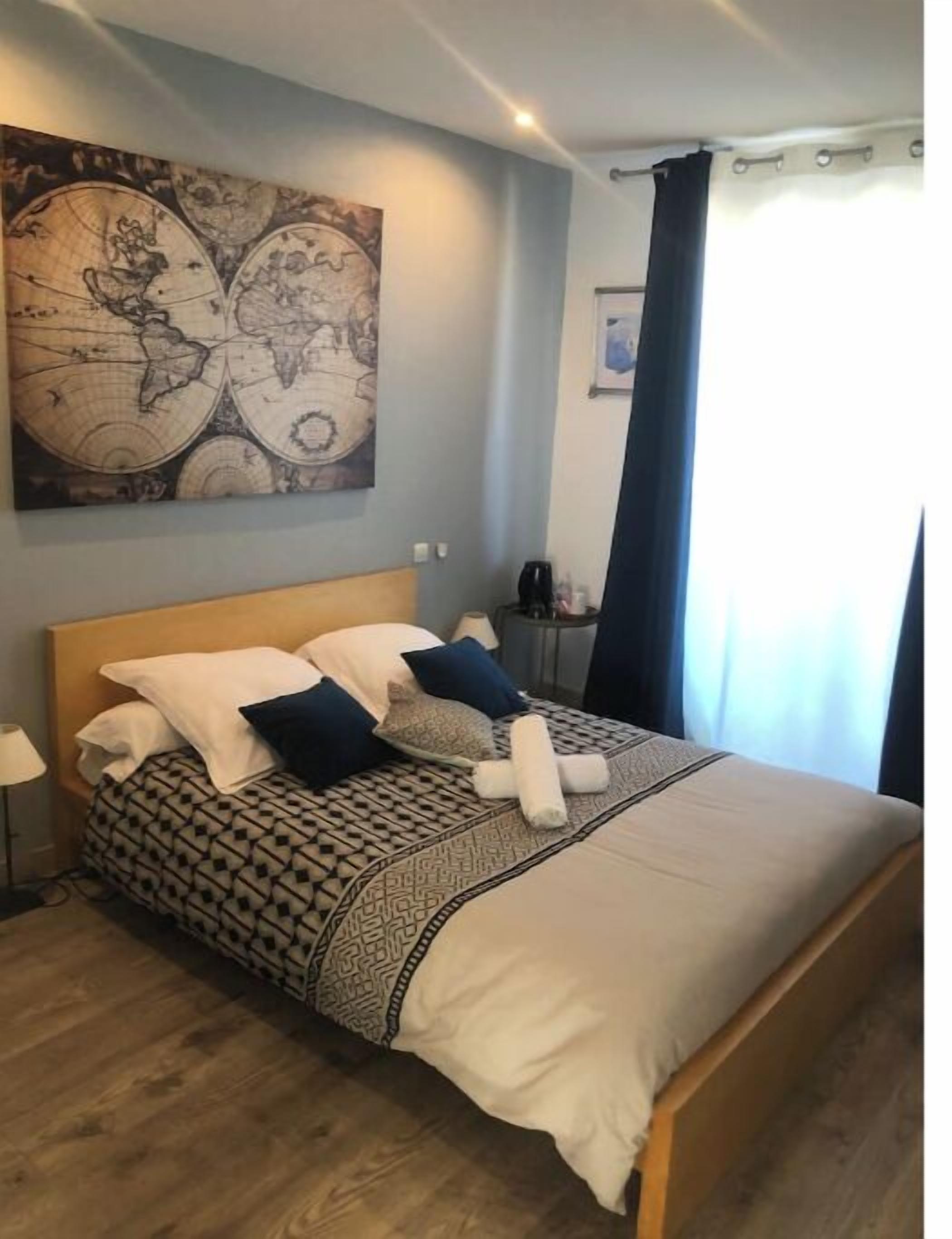 A neatly made bed with patterned bedding, a world map artwork on the wall, and a bedside table with a lamp.