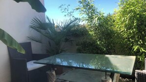 Une table à plateau en verre et à pieds en bois, entourée de verdure, avec une chaise à proximité.