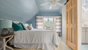 A bedroom with a bed, a ceiling fan, a window with curtains, and a wooden door. - Onset Oasis_2 min walk to beach, Sleeps 14, HUGE yard w/ lawn games & 2 grills! (Wareham)