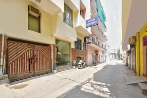 A narrow street with a gated entrance, a sign for 'Mayank Residency,' and a building with a visible entrance.