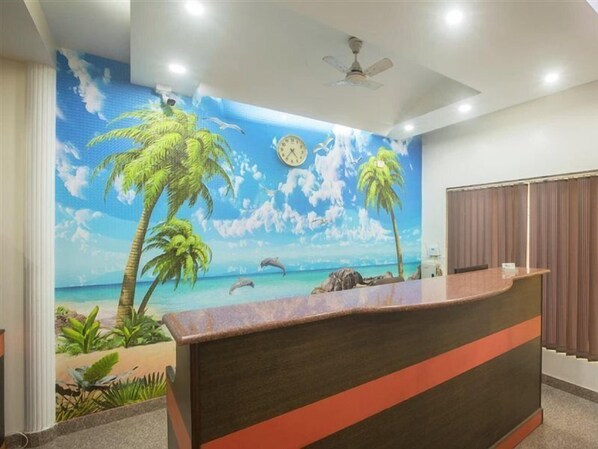 A reception area with a mural of a beach scene, a reception desk, and a ceiling fan. - Airport Hotel Mayank Residency (New Delhi)