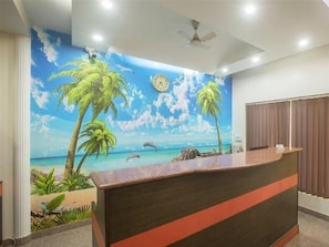 A reception area with a mural of a beach scene, a reception desk, and a ceiling fan.