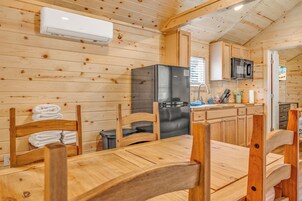 Interior de uma cabana de madeira com sala de jantar, cozinha e vista para o exterior.