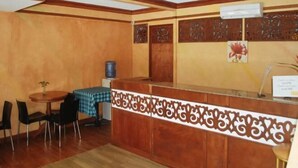 Een receptiegedeelte met een houten receptiebalie, een kleine ronde tafel met stoelen, en een waterdispenser.