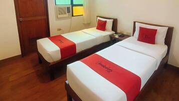 A hotel room with two beds, each with a red and white bedspread, a wooden headboard, and a nightstand with a lamp.
