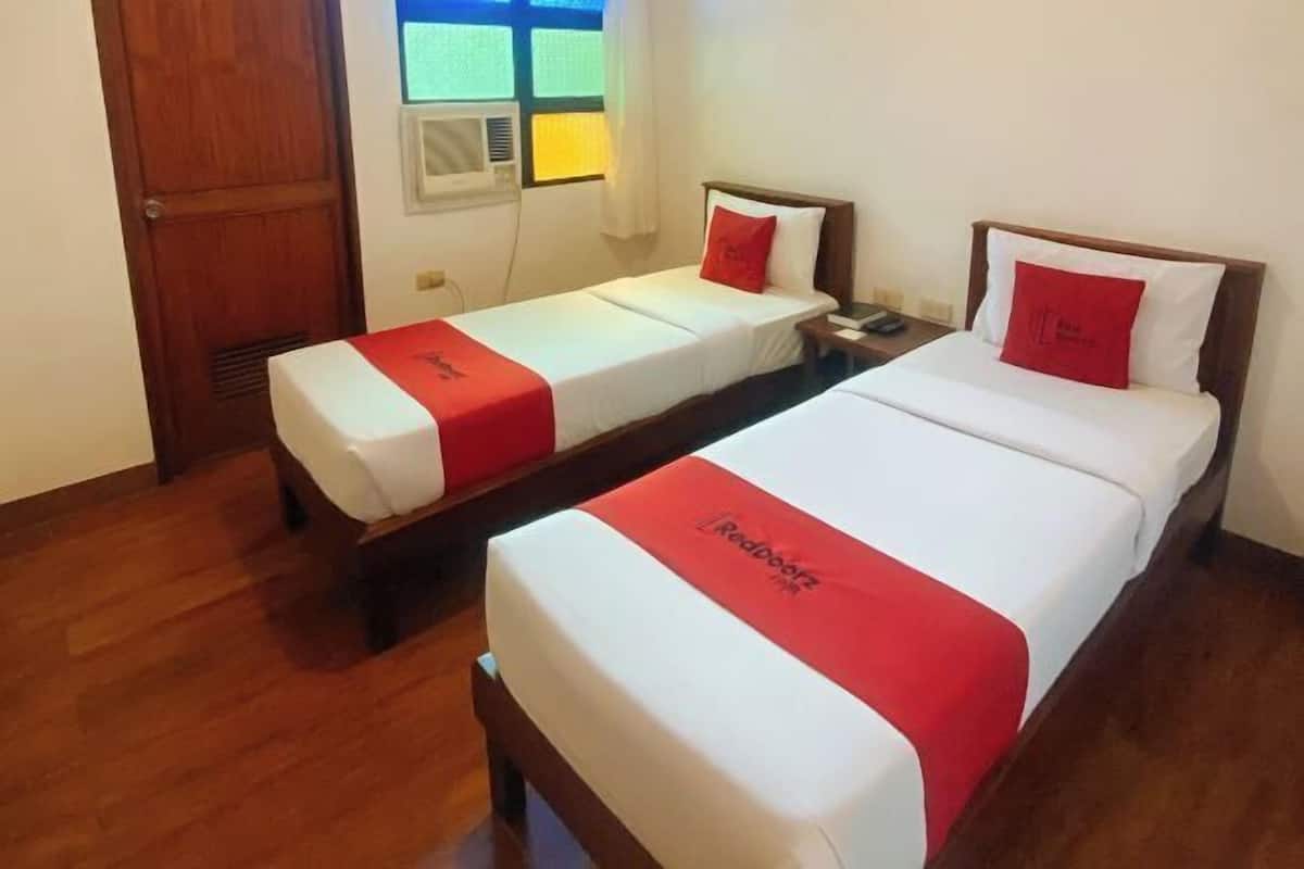Una habitación de hotel con dos camas individuales, piso de madera, una ventana con persianas y una puerta.