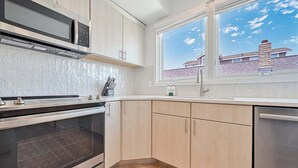 A modern kitchen with a built-in oven, microwave, and dishwasher, a window with a view of a house, and light-colored cabinetry. - Marvelous Margate family abode (Margate City)