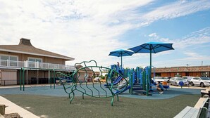 A playground with climbing structures and slides, a covered seating area, and a building with a balcony in the background. - Marvelous Margate family abode (Margate City)