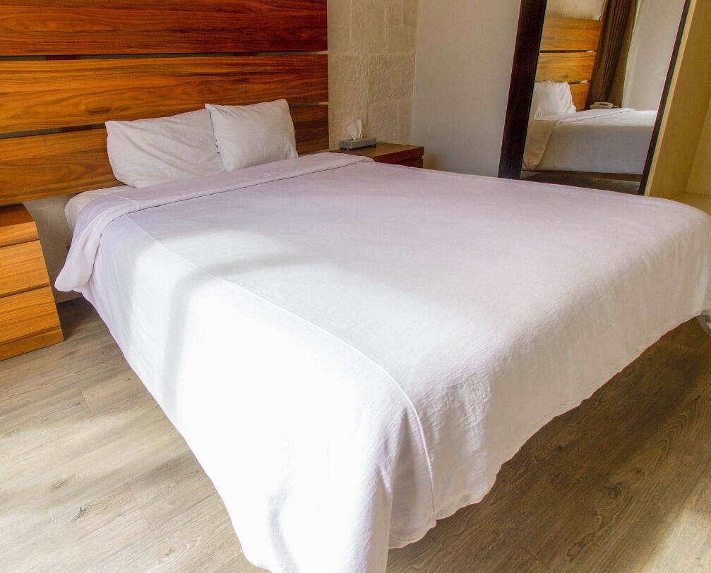 A neatly made bed with a white bedspread in a room with wooden flooring and a wooden headboard.