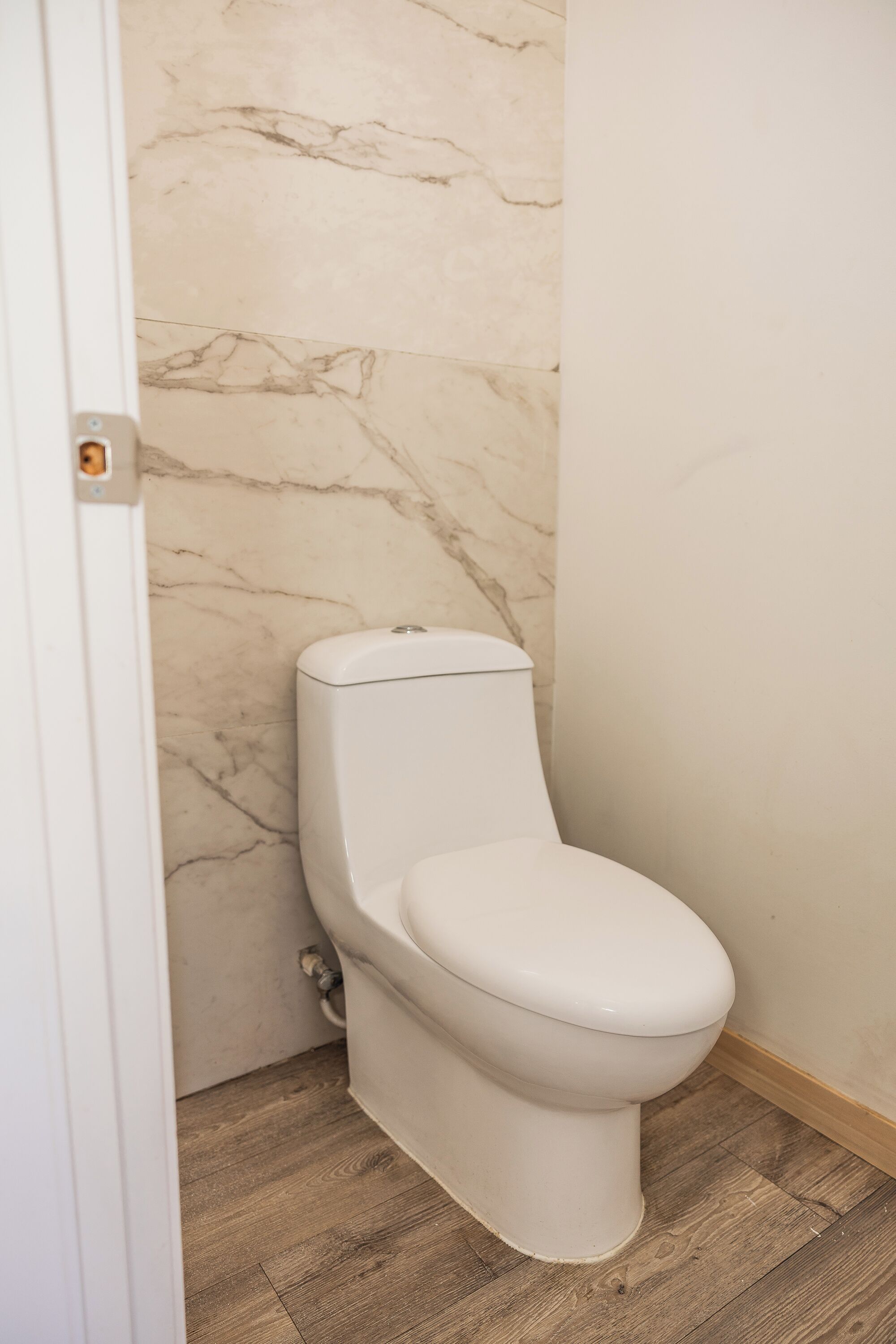 Egy fürdőszoba, amelyben WC, márványburkolatú falak és fa padló található.