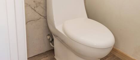 Egy fürdőszoba, amelyben WC, márványburkolatú falak és fa padló található.