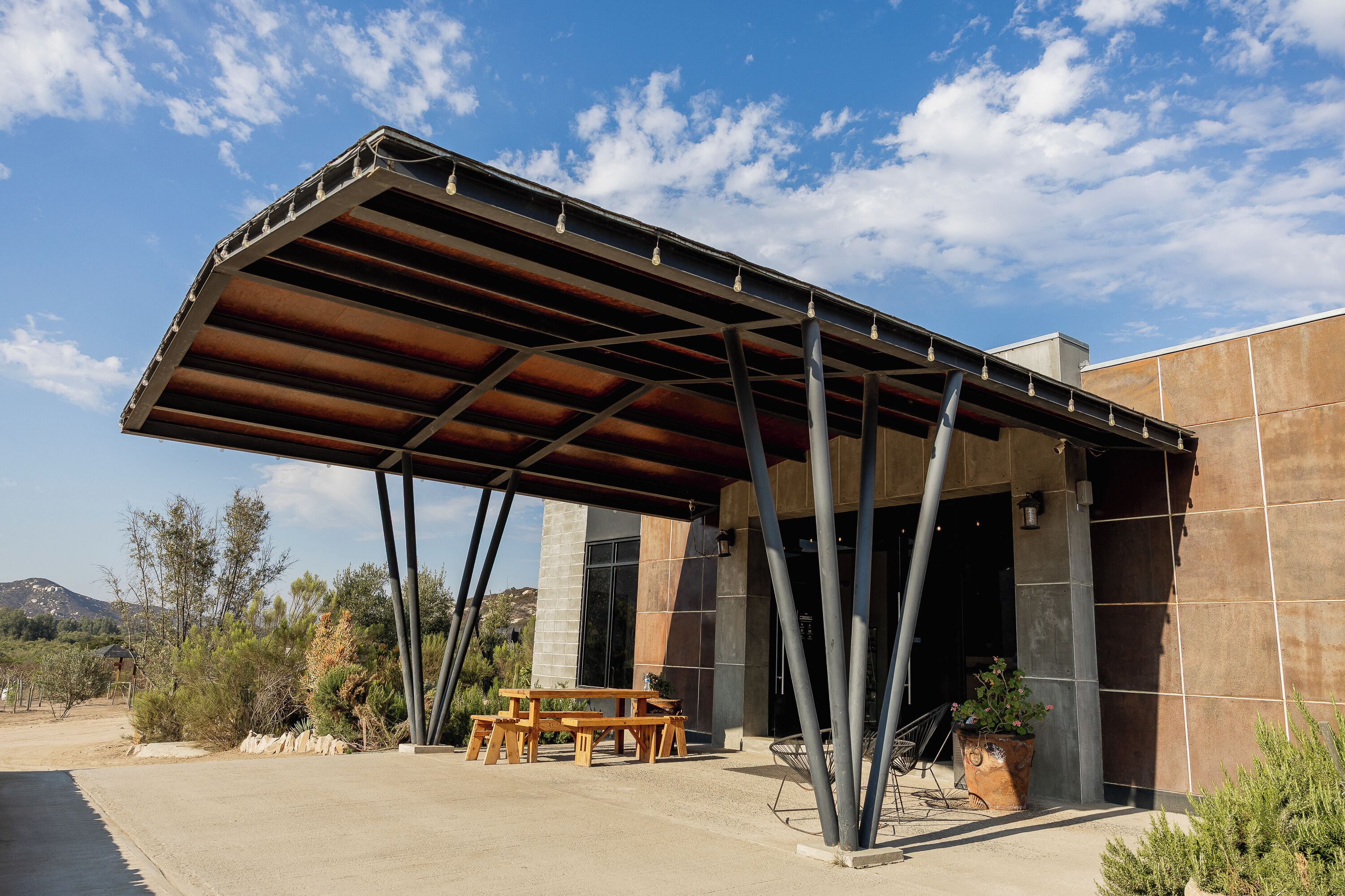 Un espacio de estar al aire libre cubierto con una mesa, sillas, una planta en maceta y un edificio de estilo arquitectónico moderno.