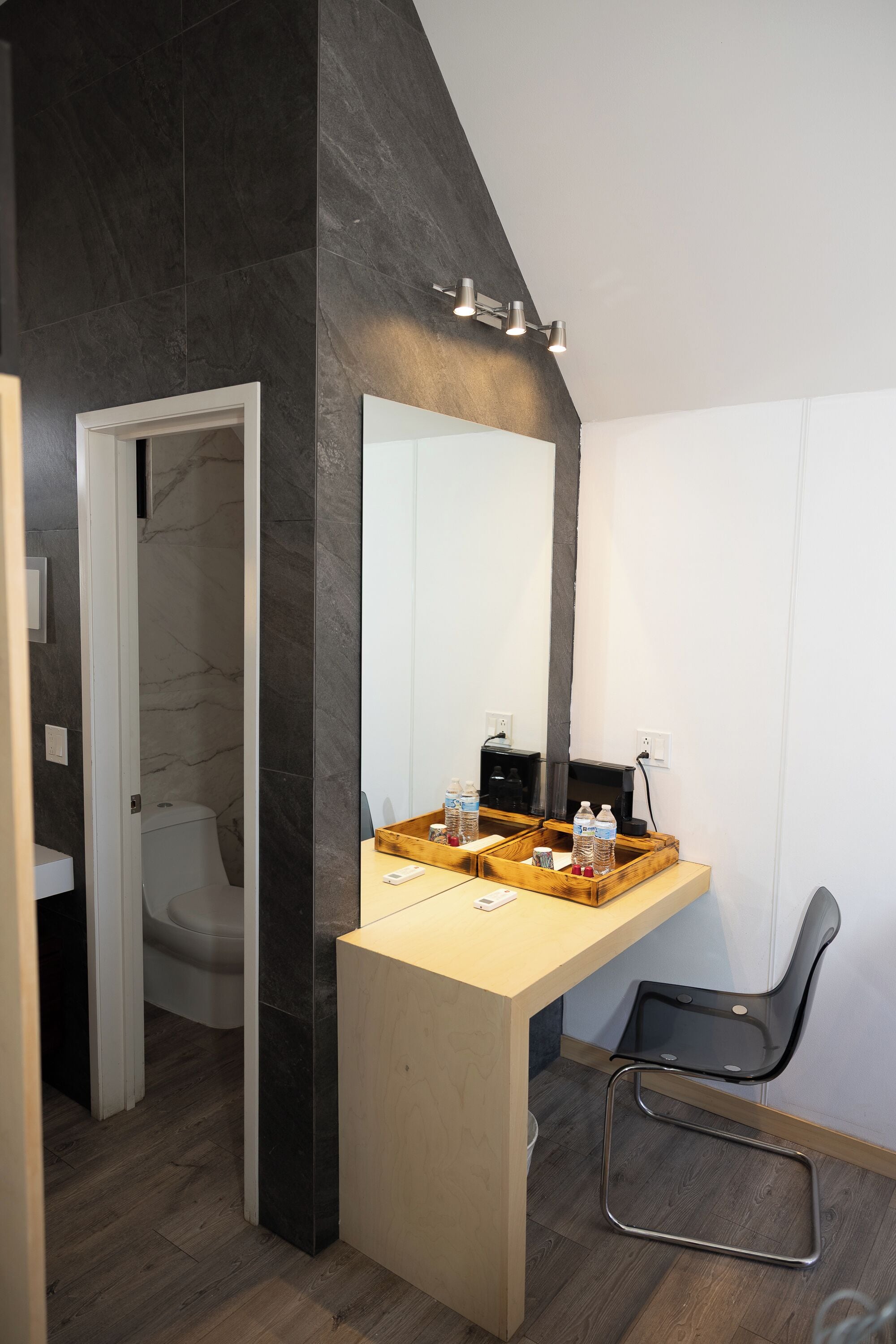 Un baño moderno con un espejo grande, un tocador de madera, una silla negra y una zona de ducha.