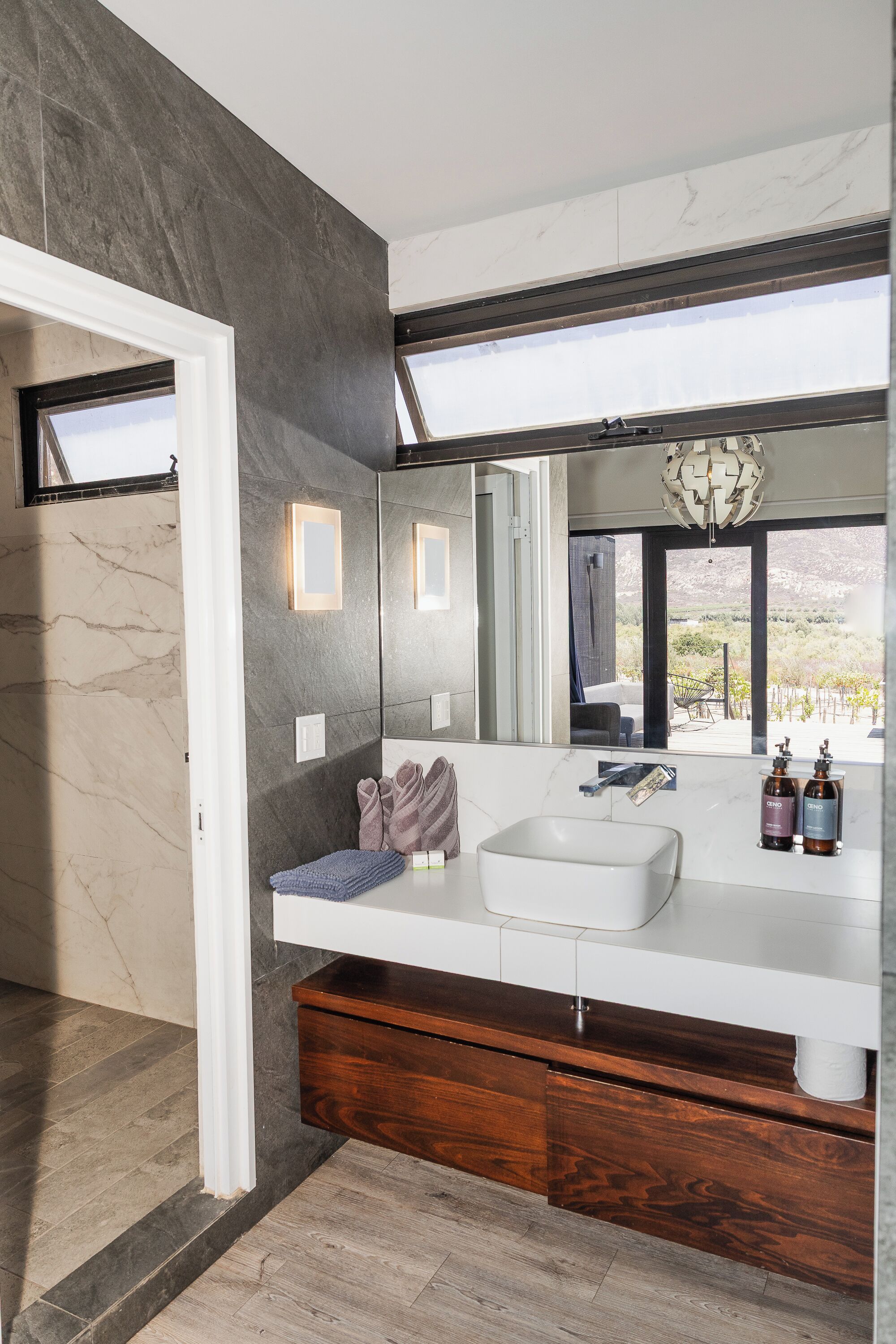 A modern bathroom with a large mirror, a white sink, and a wooden vanity.