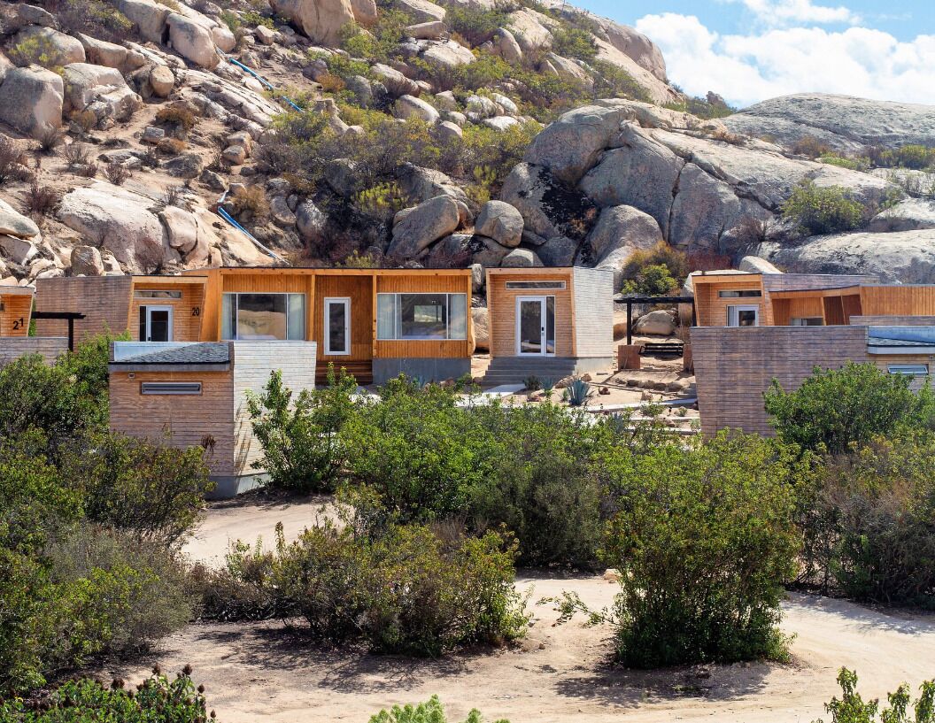 A row of modern cabins with large windows, set against a rocky hillside.