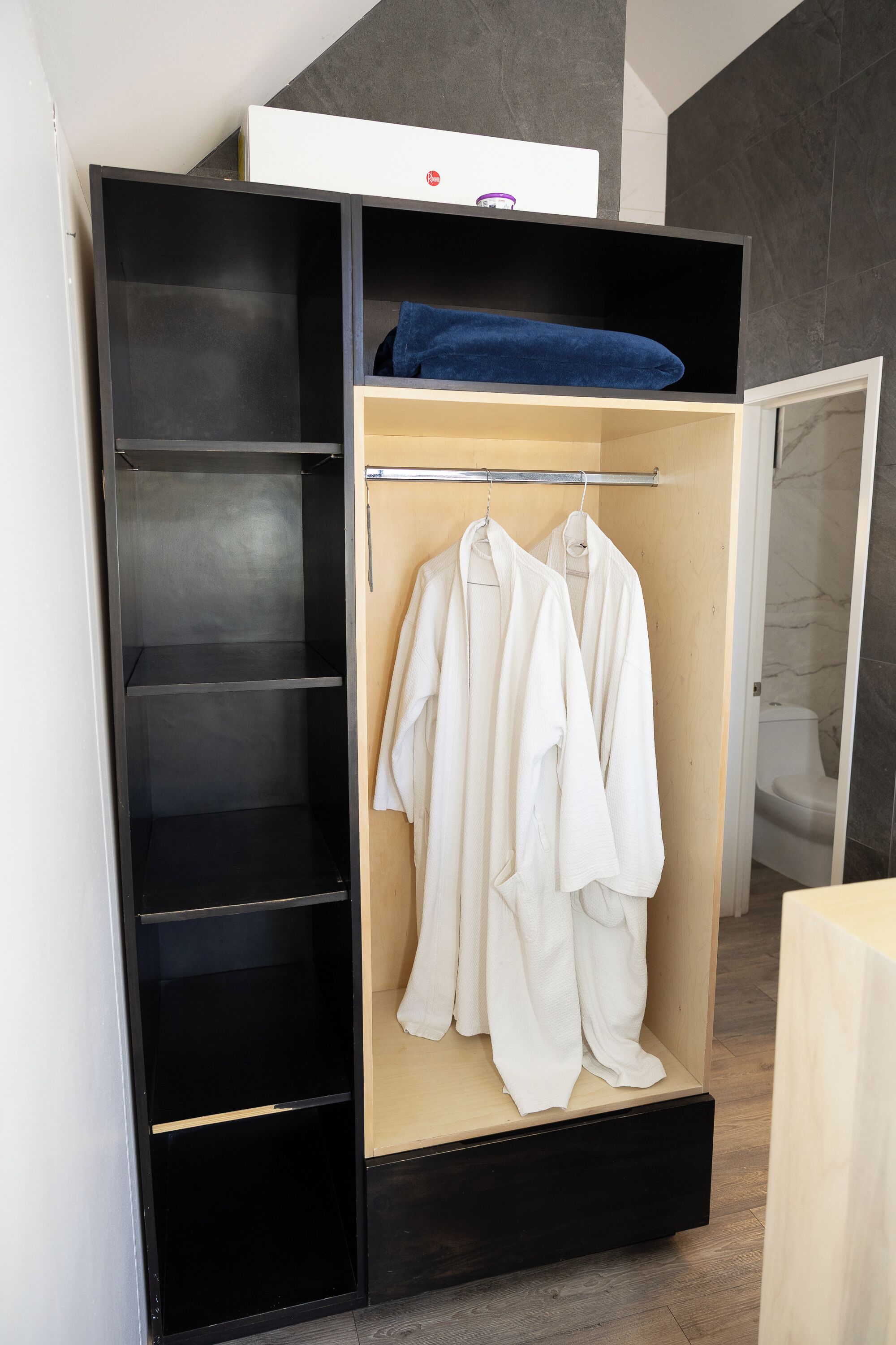 Un vestidor con estantes abiertos, una barra para colgar ropa y un pequeño armario blanco en la parte superior.
