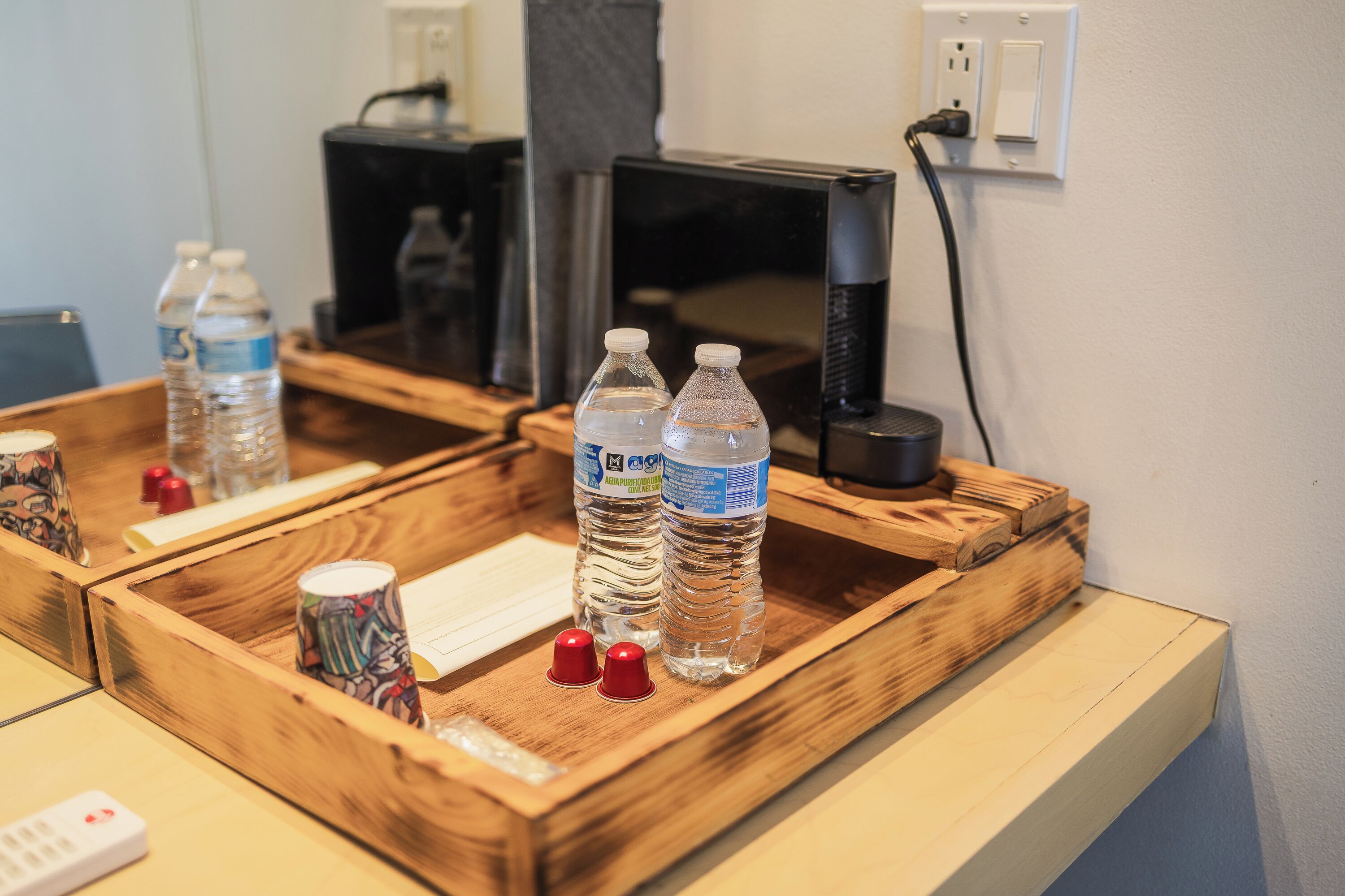 Una bandeja de madera con dos botellas de agua, un vaso de colores y un control remoto sobre un escritorio de hotel.
