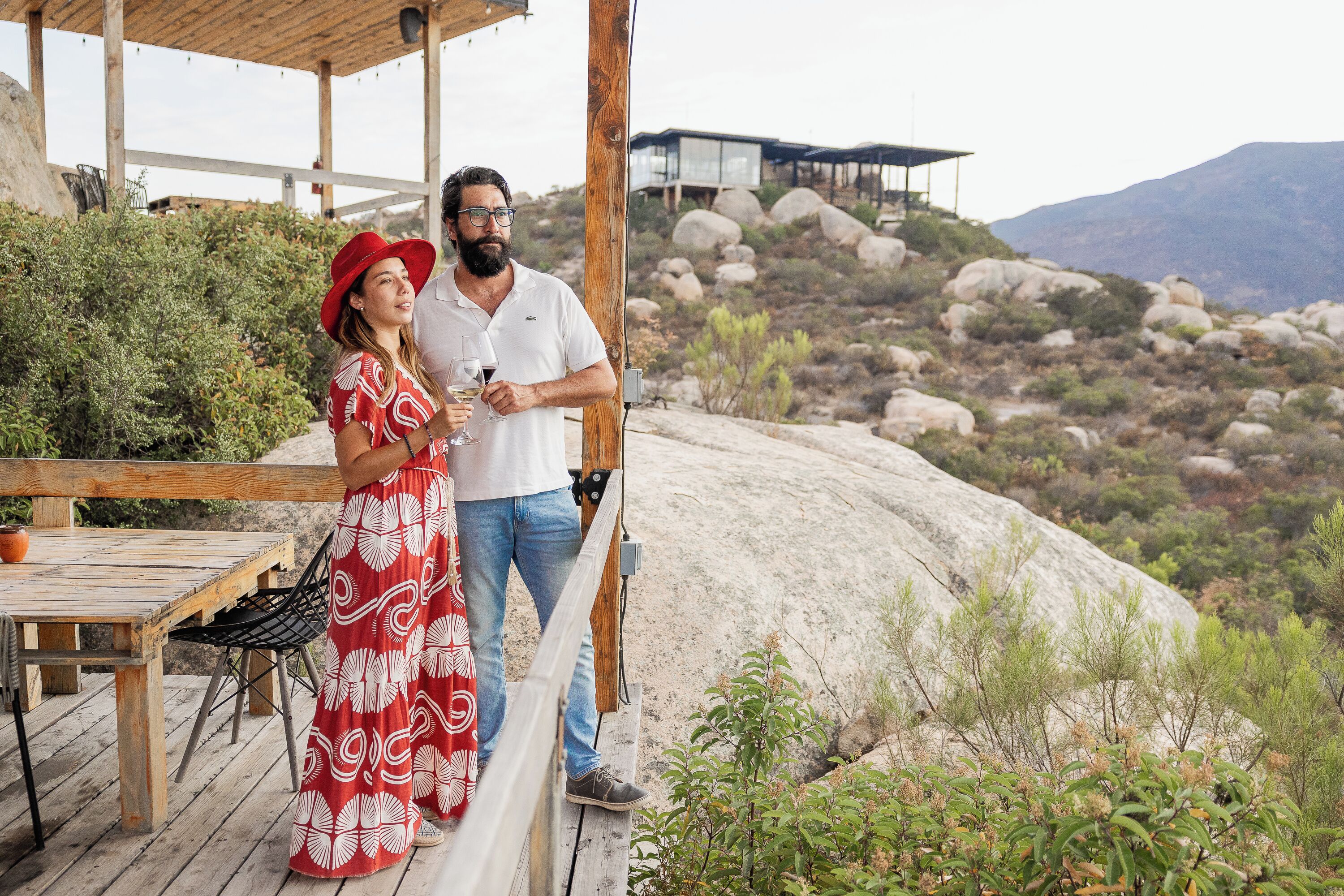 A couple standing on a wooden deck overlooking a mountainous landscape.