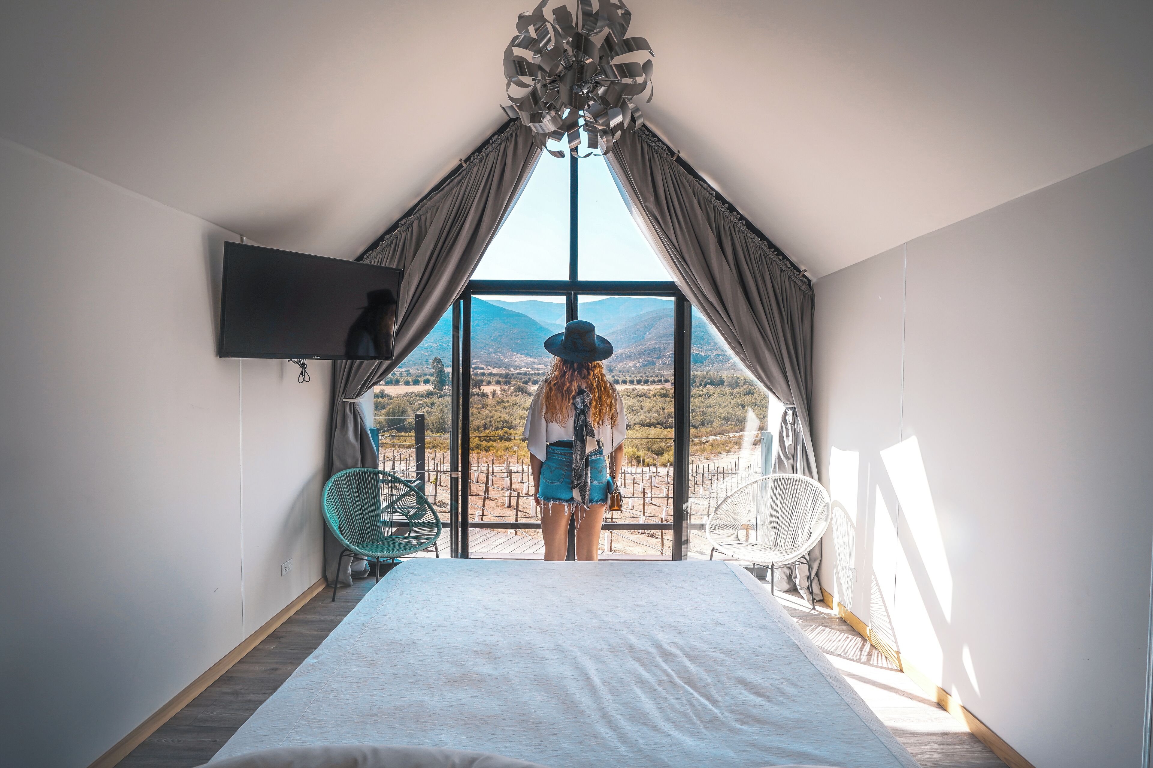 Une chambre avec une grande fenêtre, un lit et un téléviseur fixé au mur.
