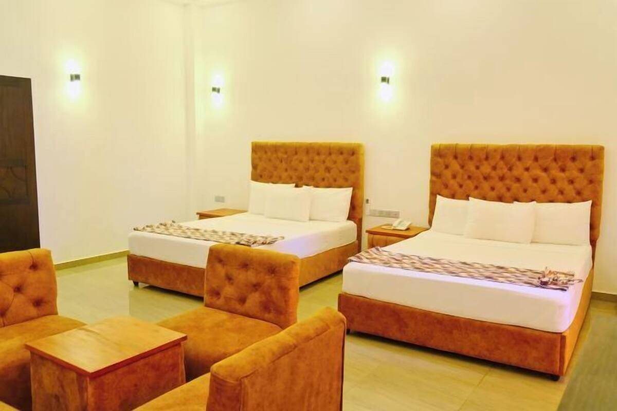 Two double beds with tufted headboards, a wooden coffee table, and matching armchairs in a hotel room.