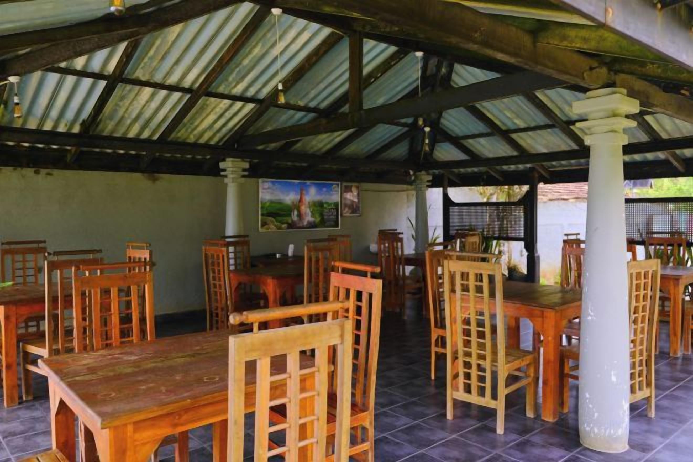 Un comedor interior con mesas y sillas de madera, suelo de baldosas y techo de metal corrugado.