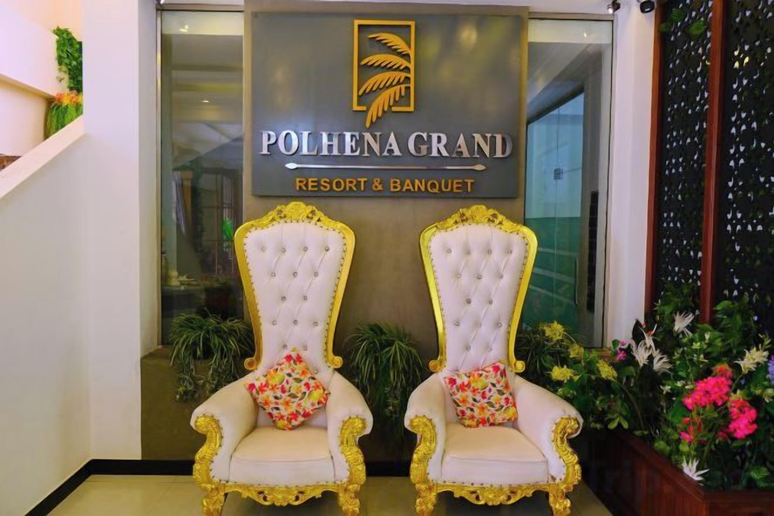 Un área de recepción con dos sillones decorados, un letrero que indica Polhena Grand Resort & Banquet, y una puerta de vidrio de acceso.