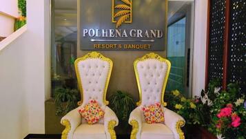 Un área de recepción con dos sillones decorados, un letrero que indica Polhena Grand Resort & Banquet, y una puerta de vidrio de acceso.
