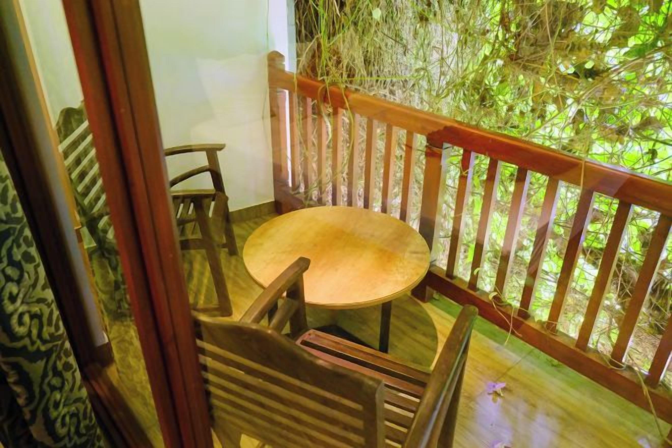 Una terraza de madera con una mesa redonda y sillas, rodeada por una barandilla de madera.
