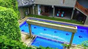 A swimming pool with a wooden deck, surrounded by lush greenery and a covered seating area. - Polhena Grand Resort & Banquet (Matara)
